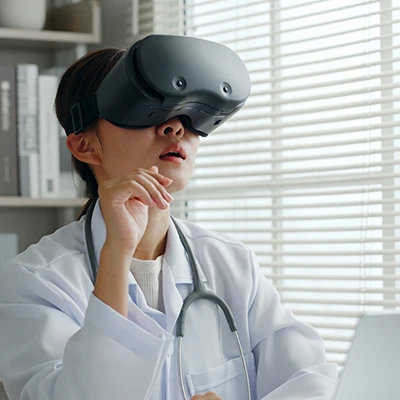 Vrouw in een witte dokterjas met een VR-bril op en stethoscoop om haar hals